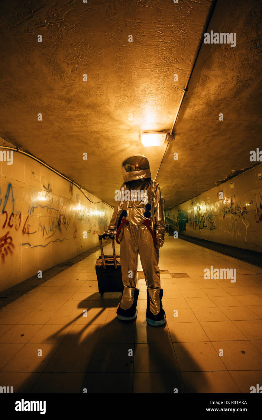 Spaceman en la ciudad en la noche de pie en el paso subterráneo con maleta con ruedas Foto de stock