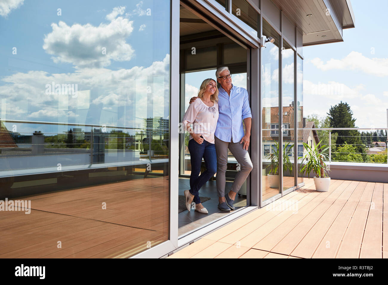 Sonriente pareja de pie en la terraza de la azotea en casa Foto de stock