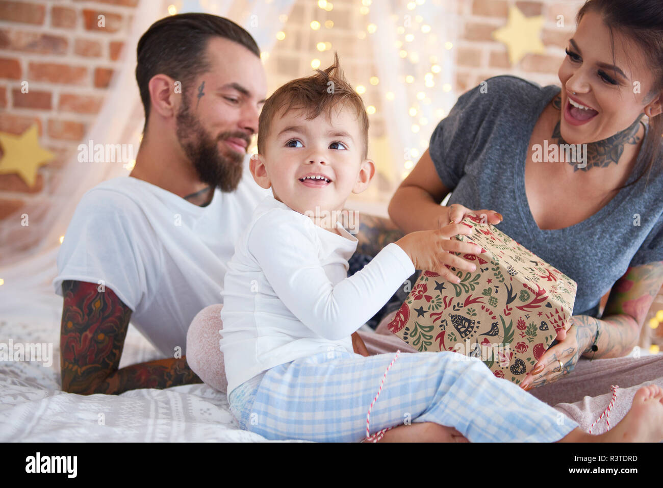 Muchacho feliz abriendo regalo de Navidad con sus padres en la cama Foto de stock