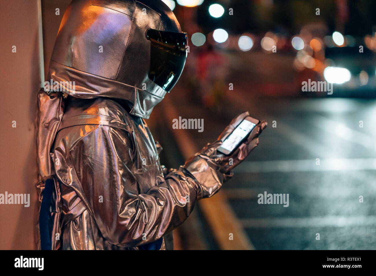 Spaceman en una calle de la ciudad de noche mediante teléfono celular Foto de stock