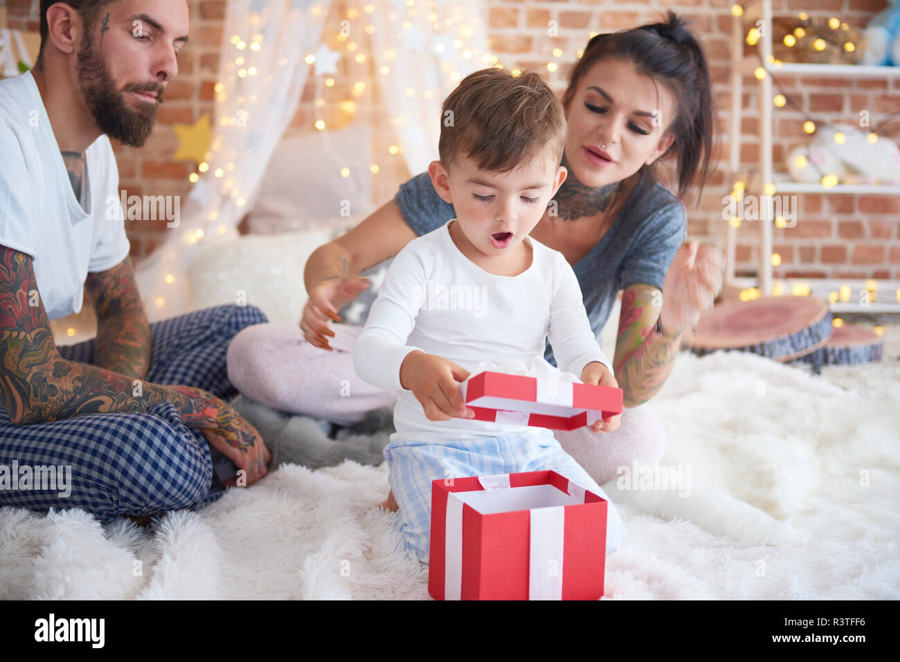 Sorprendido muchacho abriendo regalo de Navidad con sus padres en la cama Foto de stock