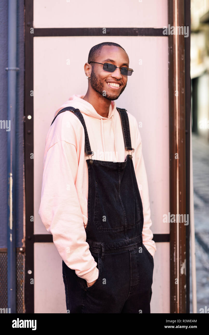 Joven negro vistiendo ropa casual y gafas de sol, sonriendo contra rosa fondo urbano. Feliz Africano joven chico con pantalones de en exterior Fotografía de stock - Alamy