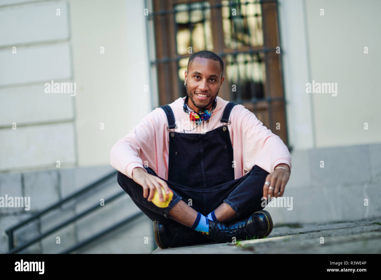 Joven negro comiendo una manzana sentado en pasos urbanos. Concepto de estilo de vida. Foto de stock