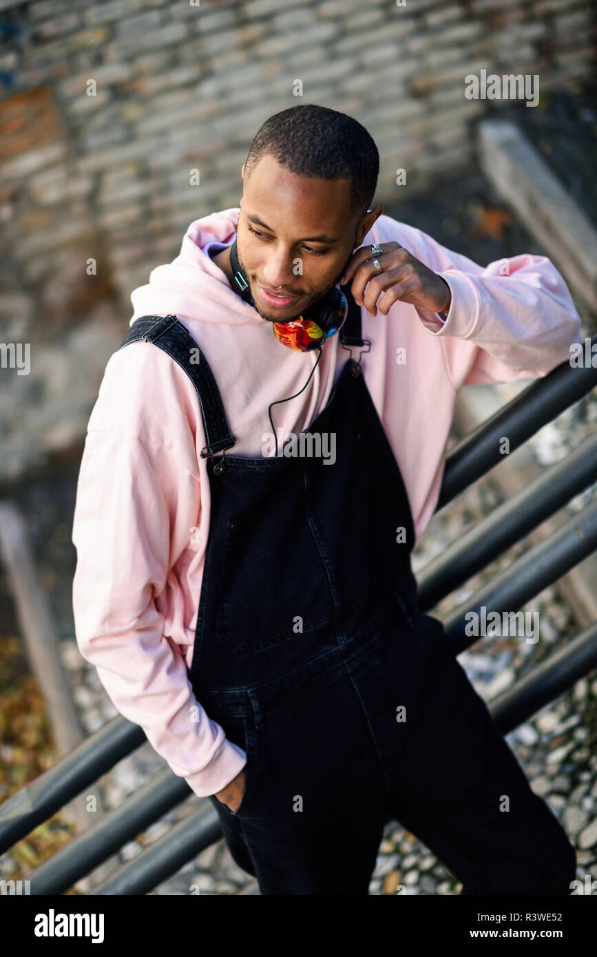 Joven negro vistiendo ropa casual sonriendo on urban escaleras. Feliz chico africano con pantalones de bib en el exterior Foto de stock