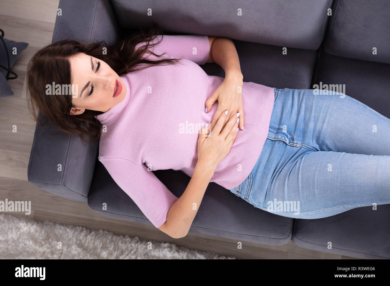 Mujer joven tumbado en el sofá sufriendo de dolor de estómago en casa Foto de stock