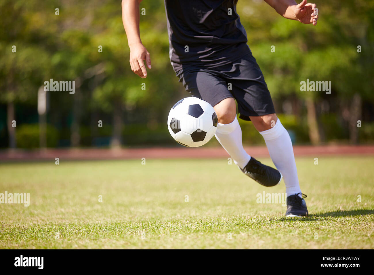Primer plano de los pies del jugador de fútbol asiático manejar el balón en el campo de fútbol. Foto de stock