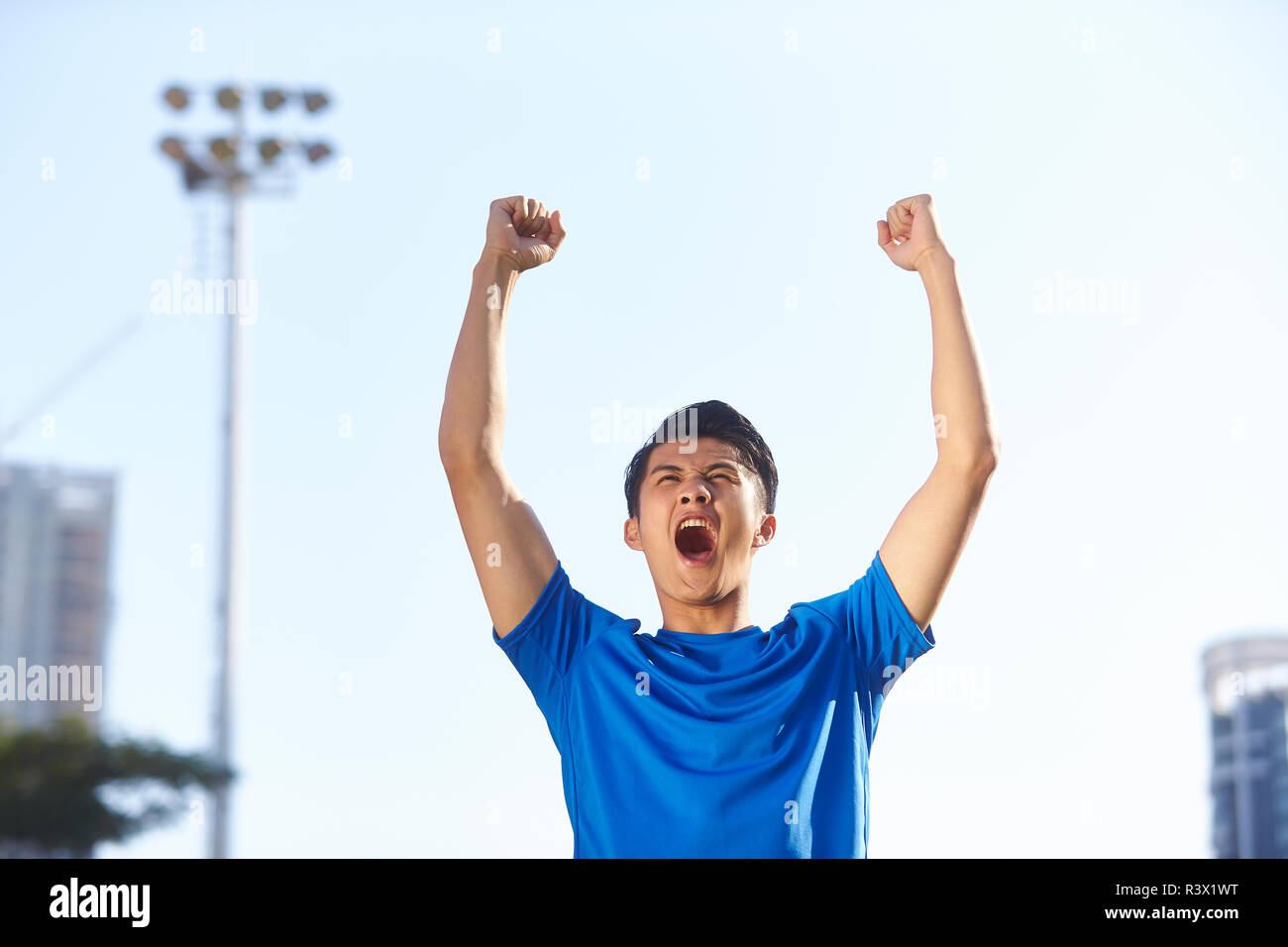 Joven atleta masculino asiático celebrando la victoria con los puños y los brazos levantados Foto de stock