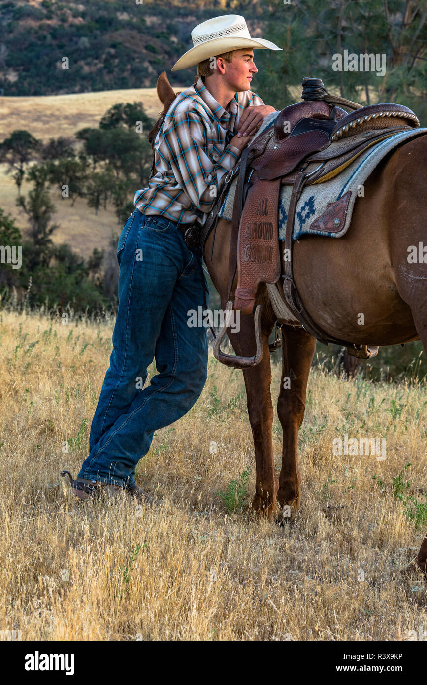 California, Estados Unidos, Parkfield, V6 Rancho vaquero joven de pie junto  a su caballo recostado en su montura (MR Fotografía de stock - Alamy