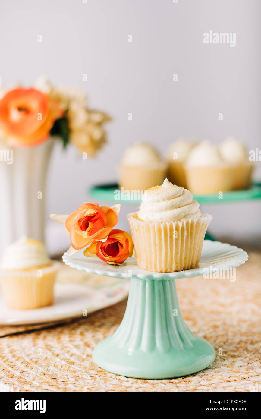 Bonita pantalla de pastelitos de vainilla con flores sobre una mesa Foto de stock