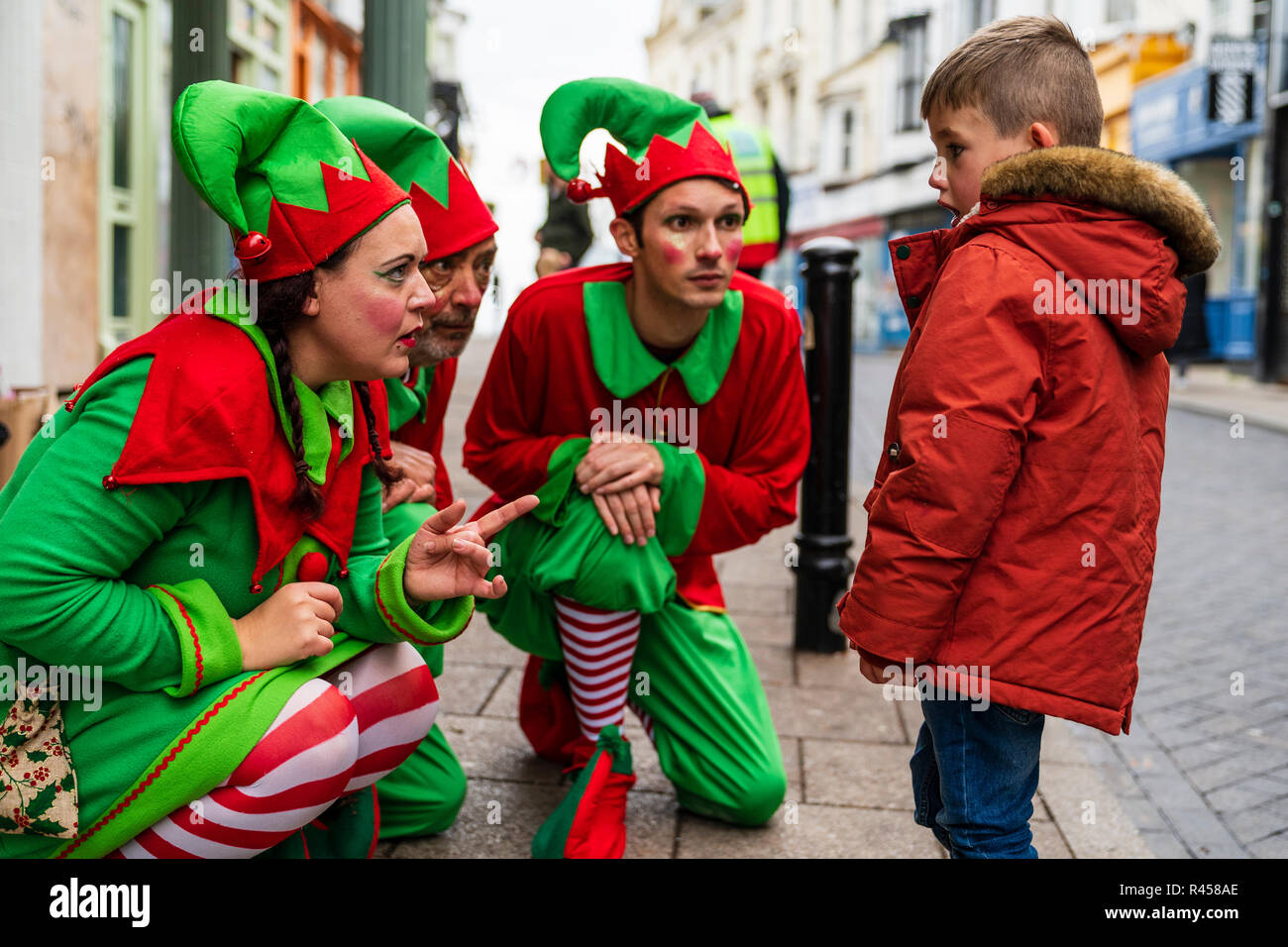 Tres personas vestidas como Santa's elfos arrodillado hablando a un niño, joven, que está mirando horrorizados con la boca abierta en ellos. Escena callejera durante un evento de Navidad en la ciudad de Ramsgate. Foto de stock