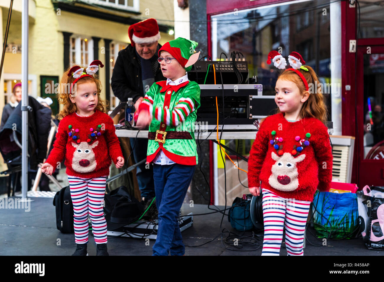 Tres jóvenes niños caucásicos, un muchacho, dos niñas de 6-7 años de edad, vestidos como elfos de Santa Claus en el escenario al aire libre bailando durante el evento de Navidad. Foto de stock