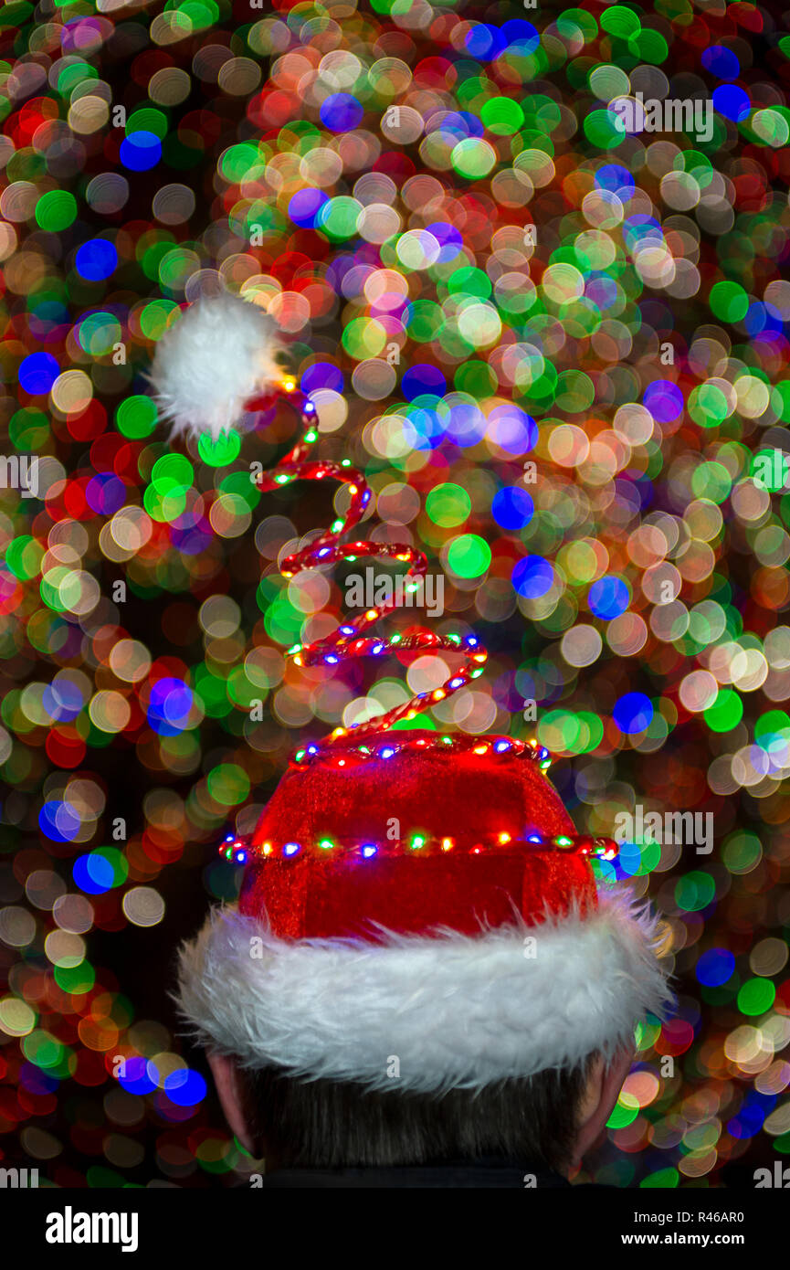 Gorro de Papá Noel brillante delante de coloridas luces bokeh abstracta del gigante árbol de Navidad Foto de stock