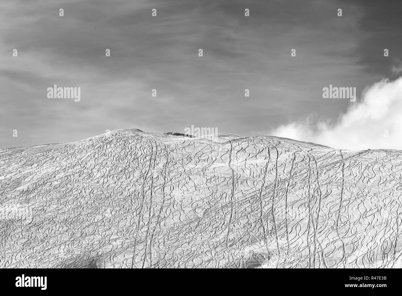 Vista en blanco y negro con nieve fuera de pista pendiente para freeride con trazas de esquís, snowboards y cielo con nubes en sun día de invierno. Montañas del Cáucaso Foto de stock