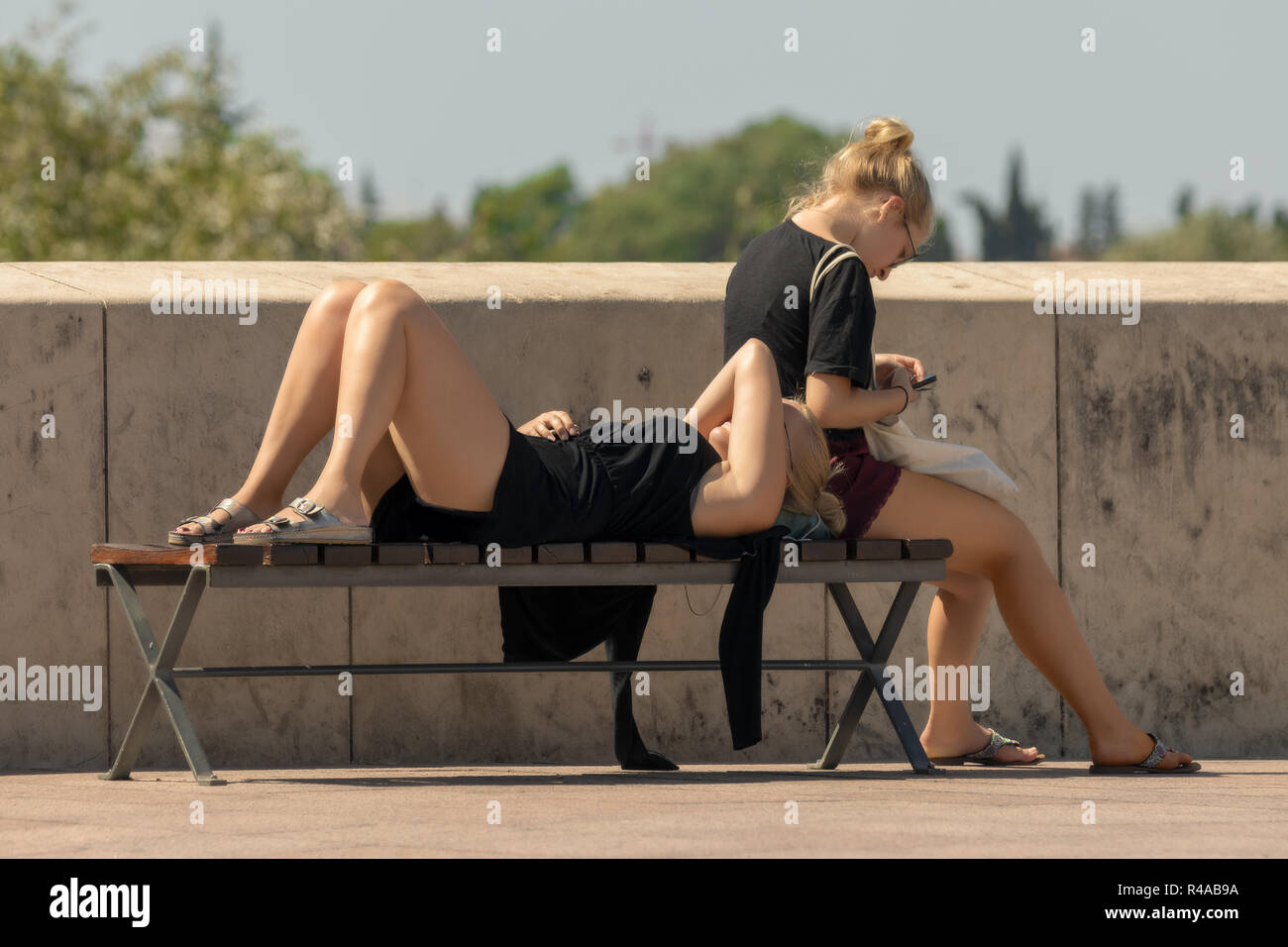 Hermanas turistas descansando en el sol tumbado y sentado en un banco. Foto de stock