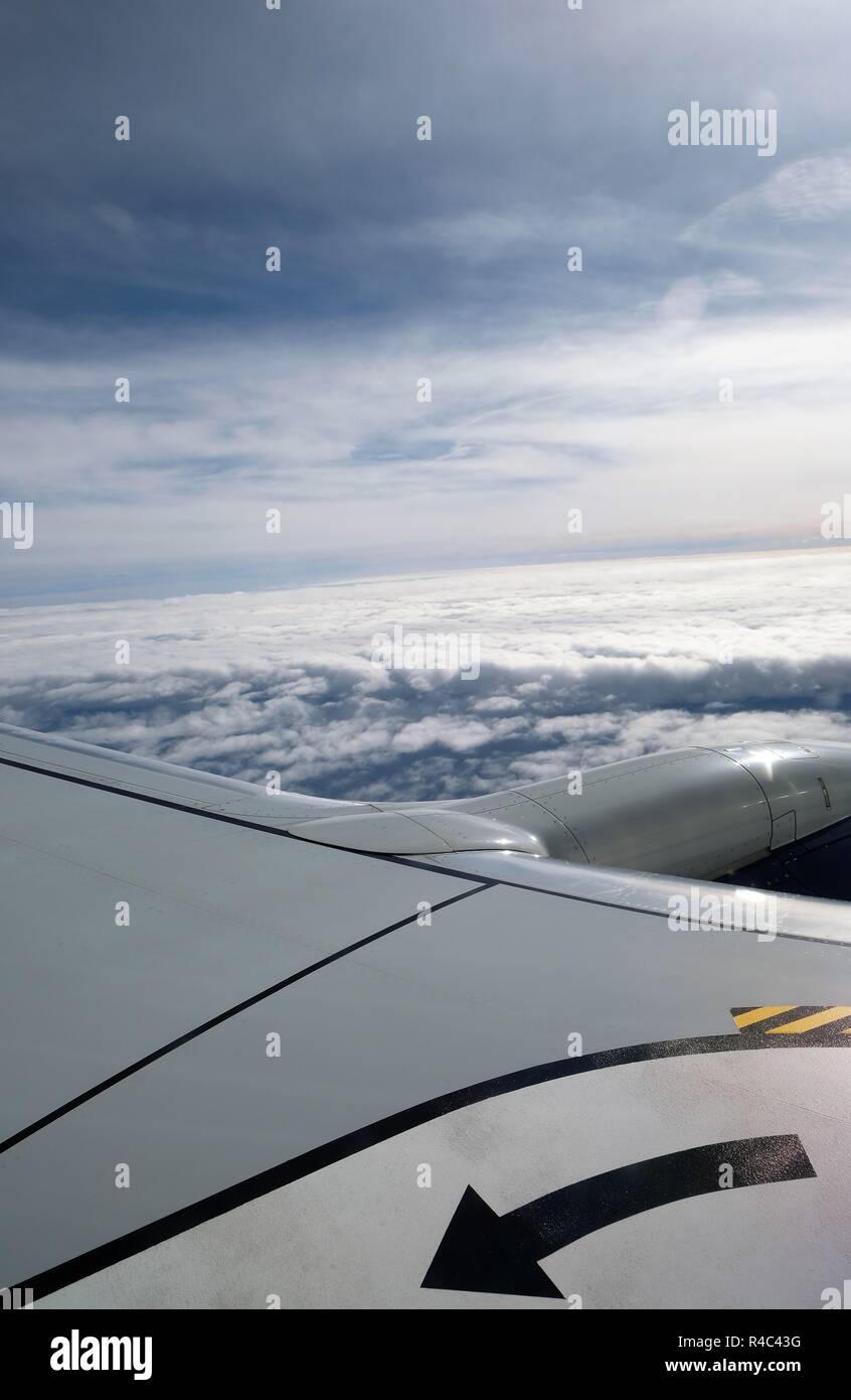 Vista de las nubes y el cielo desde un avión; ventana vista parcial del ala y motor de turbina. Foto de stock