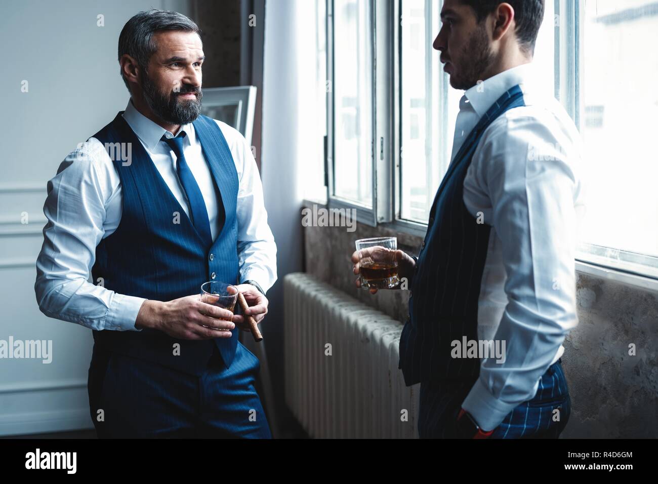 Relajante. Longitud total de dos jóvenes hombres guapos en trajes  celebración gafas y mirando el uno al otro mientras descansa en el interior  Fotografía de stock - Alamy