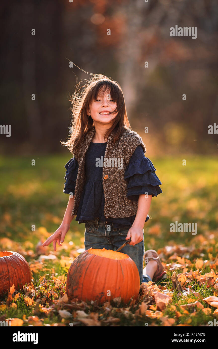 Chica sonriente tallando una calabaza de Halloween en el jardín, Estados Unidos Foto de stock