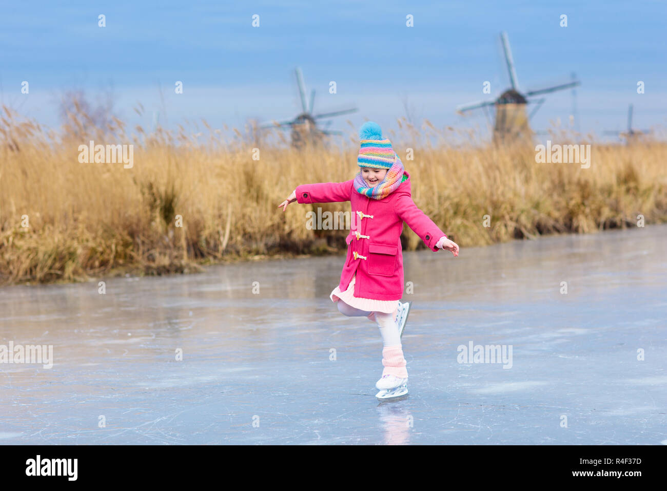 Niño patinando sobre hielo congelado canal con molinos de viento y nieve en Holanda. Niña con patines sobre hielo natural en días fríos de invierno en los Países Bajos. K Foto de stock