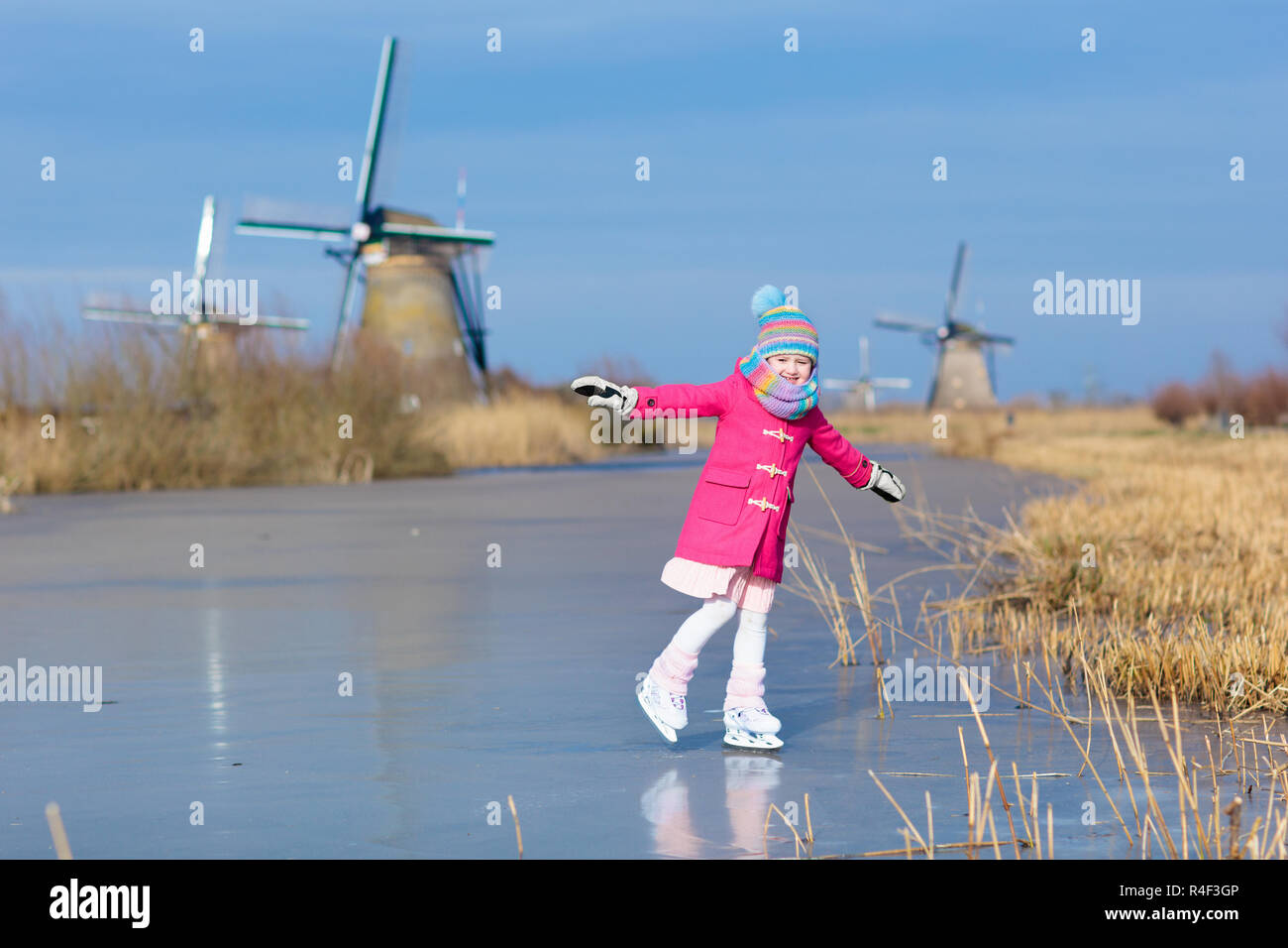 Niño patinando sobre hielo congelado canal con molinos de viento y nieve en Holanda. Niña con patines sobre hielo natural en días fríos de invierno en los Países Bajos. K Foto de stock