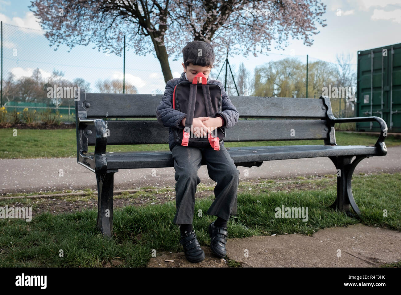 Reino Unido, niño sentado solo en una banca del parque, sintiéndose intimidado Foto de stock