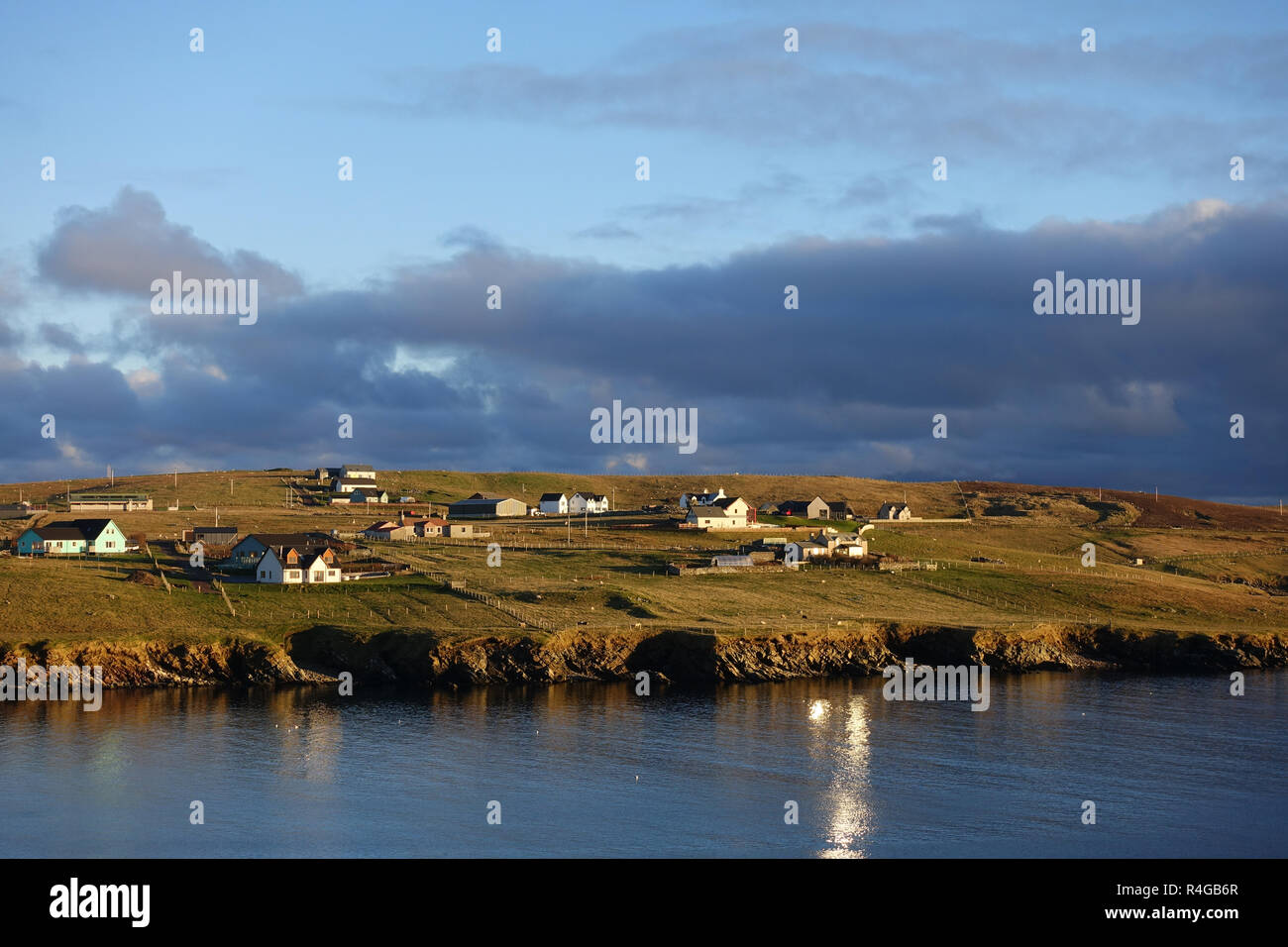 Bajo la luz en invierno Hoswick Sandwick Shetland con hogares alrededor de los acantilados y la costa de la aldea Foto de stock