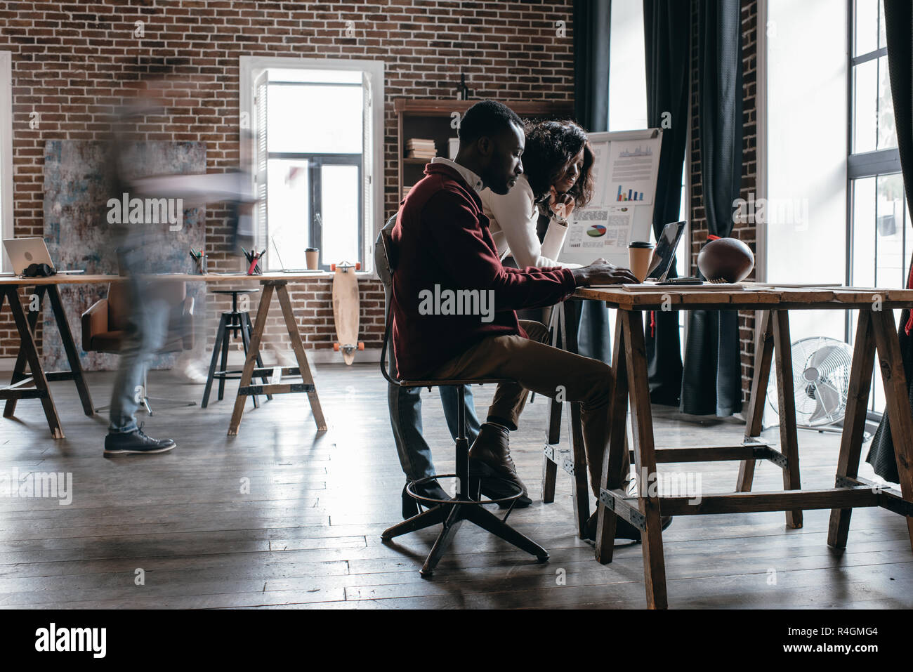 Pareja americana africana de empresarios en la mesa de trabajo informal con los colegas en el desenfoque de movimiento en la oficina loft moderno Foto de stock