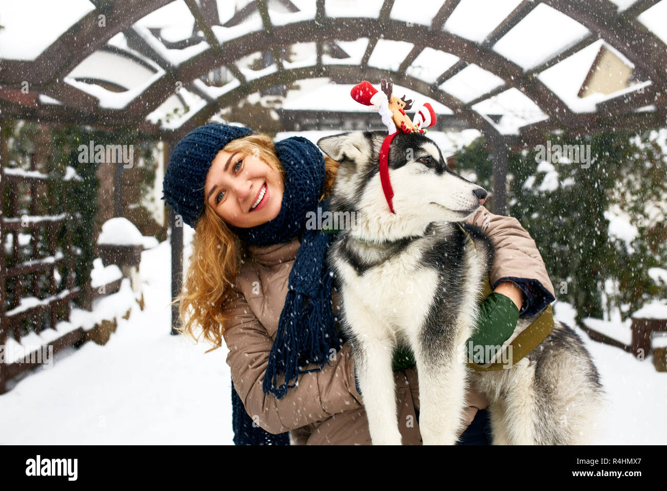 Atractiva mujer caucásica auténtico abrazos gracioso malamute perro vistiendo santa queridos astas de navidad. Rizado mujer sonriente divirtiéndose con cachorro huskie en año nuevo. El Pet es el mejor regalo para las vacaciones. Foto de stock