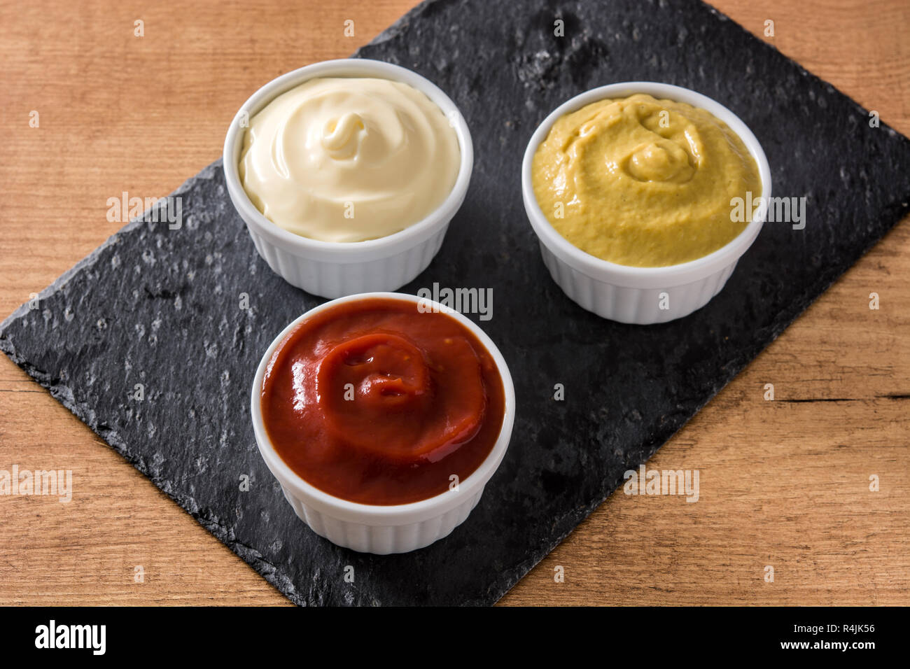El ketchup, mostaza y mayonesa en un bowls en pizarra negra Fotografía