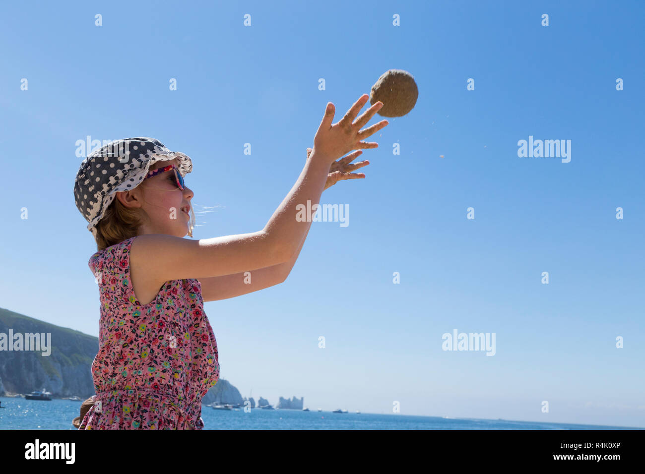 Niña de 8 años / 8 años, jugando a tirar una bola de arena / juega en la  playa en Alum Bay en la Isla de Wight, Reino Unido. Llevar sombrero y