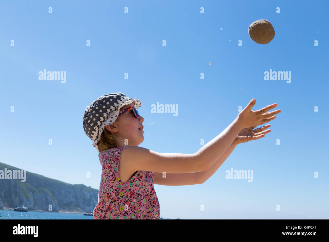 Niña de 8 años / 8 años, jugando a tirar una bola de arena / juega en la  playa en Alum Bay en la Isla de Wight, Reino Unido. Llevar sombrero y