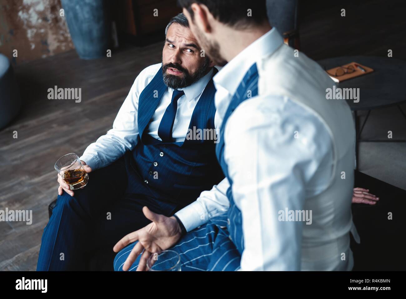 Los hombres con estilo. Dos hombres guapos en trajes celebración gafas y  mirando el uno al otro mientras descansa en el interior Fotografía de stock  - Alamy