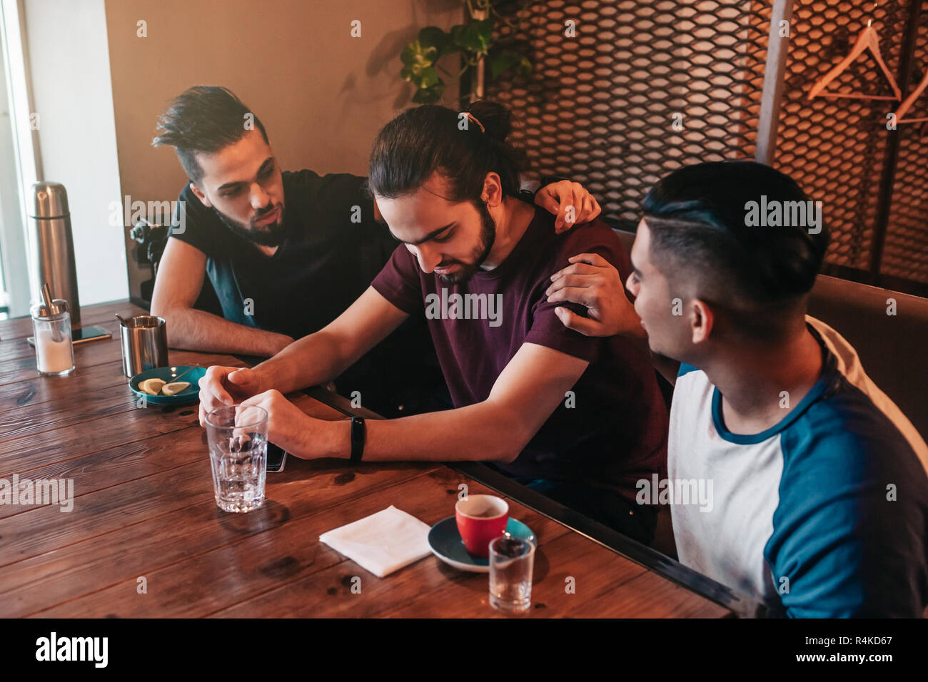 Los hombres jóvenes de apoyo animan a sus desolados amigo. Arabian chicos animarle y aconsejarle en el restaurante. Concepto de amistad. Foto de stock