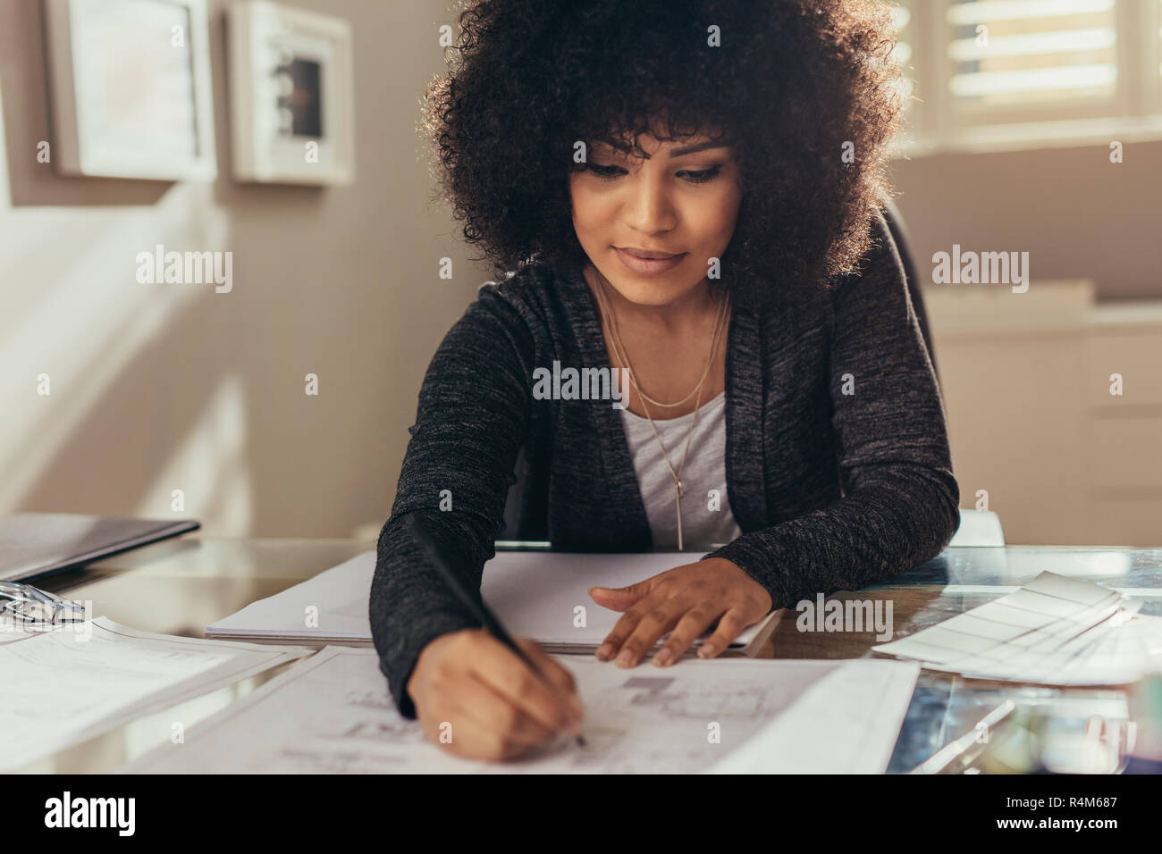 Arquitecto de mujeres trabajando en nuevos planes de construcción en su escritorio. Mujer Africana con el cabello rizado haciendo algunos cambios en el plano de planta. Foto de stock