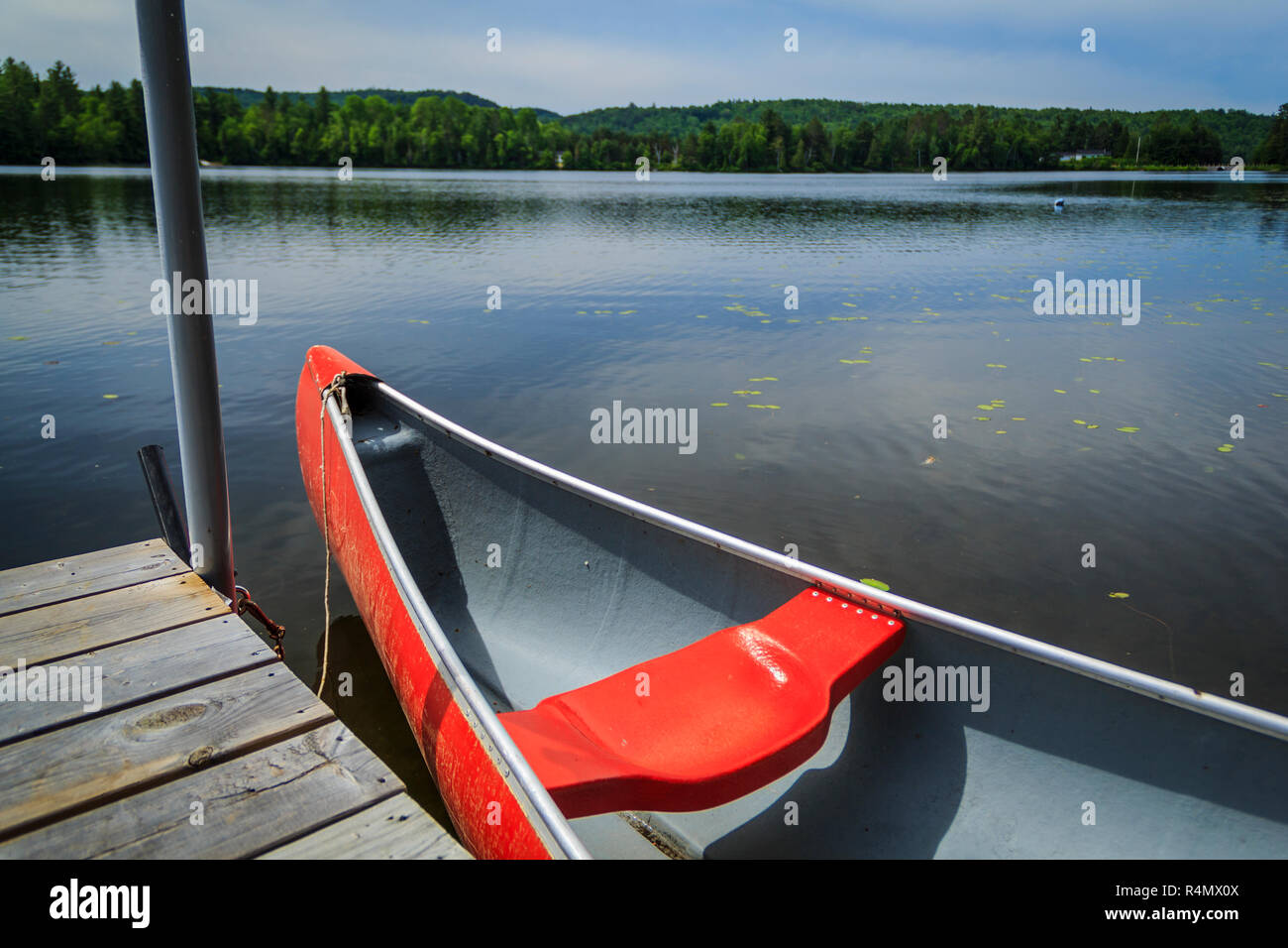 Canoa rojo atado a un muelle en las tranquilas aguas de un lago en el norte de Ontario, Canadá Foto de stock