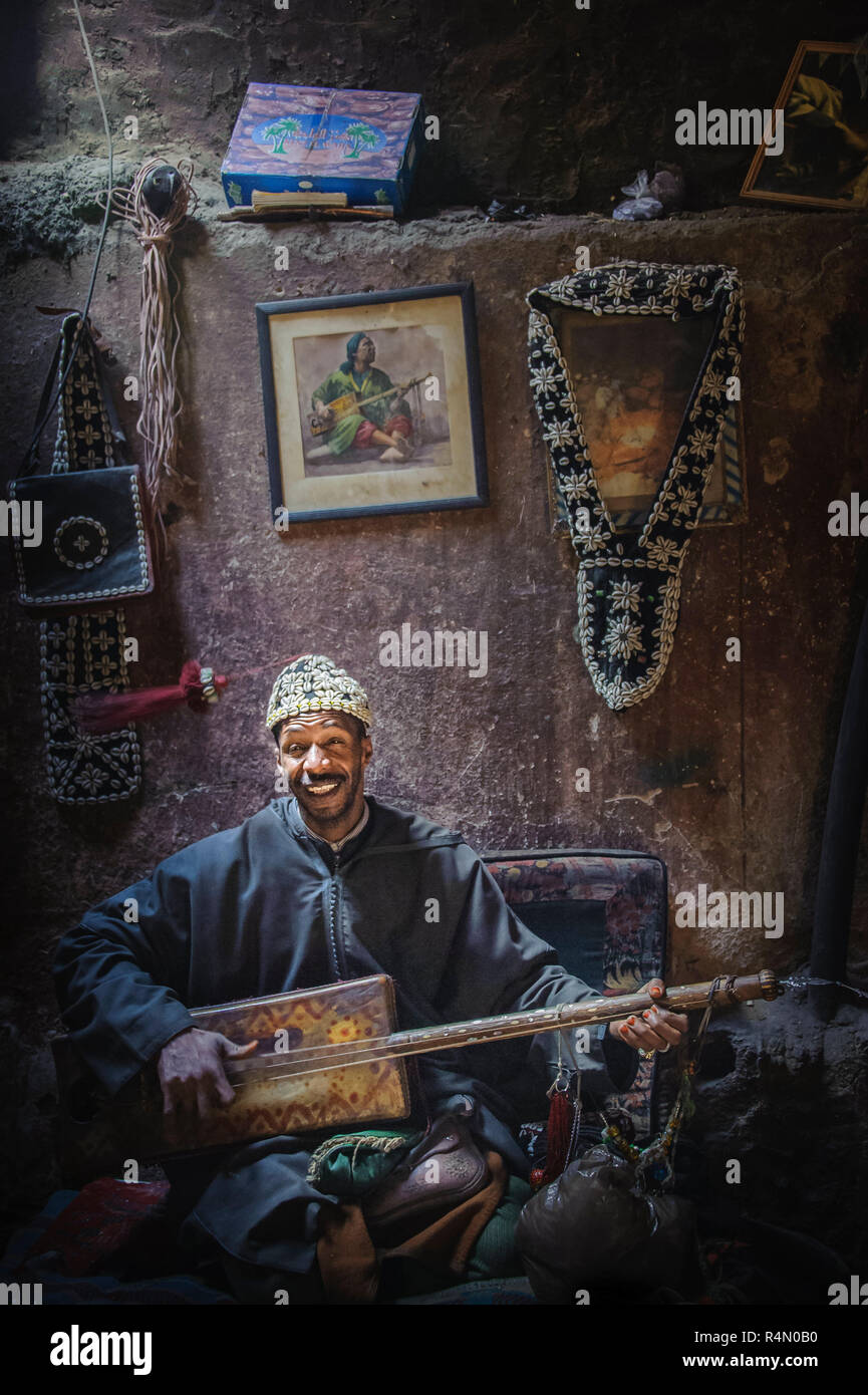 18-04-11. Marrakech, Marruecos. Un músico sentado piernas cruzadas y reproducción de una tradicional de tres cuerdas de guembri instrumento musical. Él lleva un fez hat Foto de stock