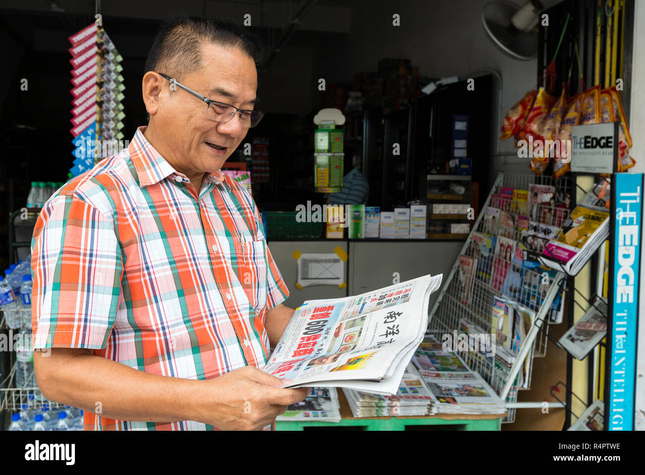 Hombre de mediana edad leyendo el periódico en idioma chino en Ipoh, Malasia. Foto de stock