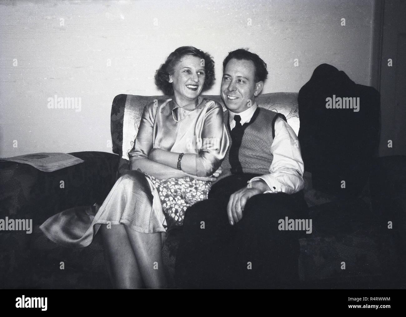 1950s, históricos, feliz esposo y esposa sentados juntos dentro de una habitación en un pequeño sofá de dos plazas. Foto de stock