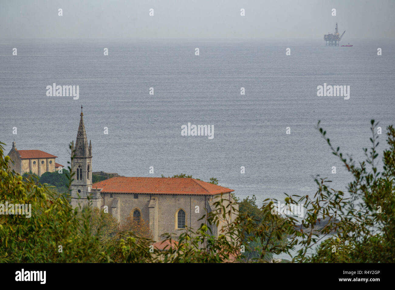Mundaka iglesia con gas de la plataforma oceánica en el horizonte Foto de stock