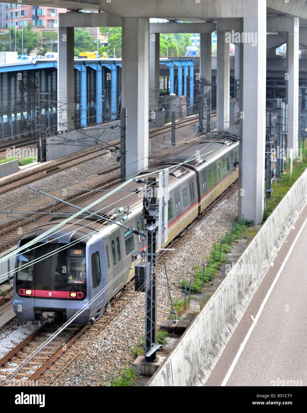 Un tren MTR corre en una pista de tierra bajo el puente carretero, Sham Shui Po, Hong Kong Foto de stock