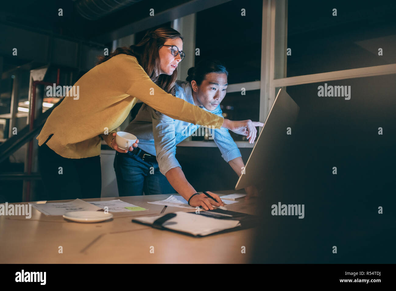 empresaria mostrando algo en la pantalla de la computadora a su socio de negocios. hombre de negocios y mujer que trabajan juntos tarde en la noche en la oficina. Foto de stock