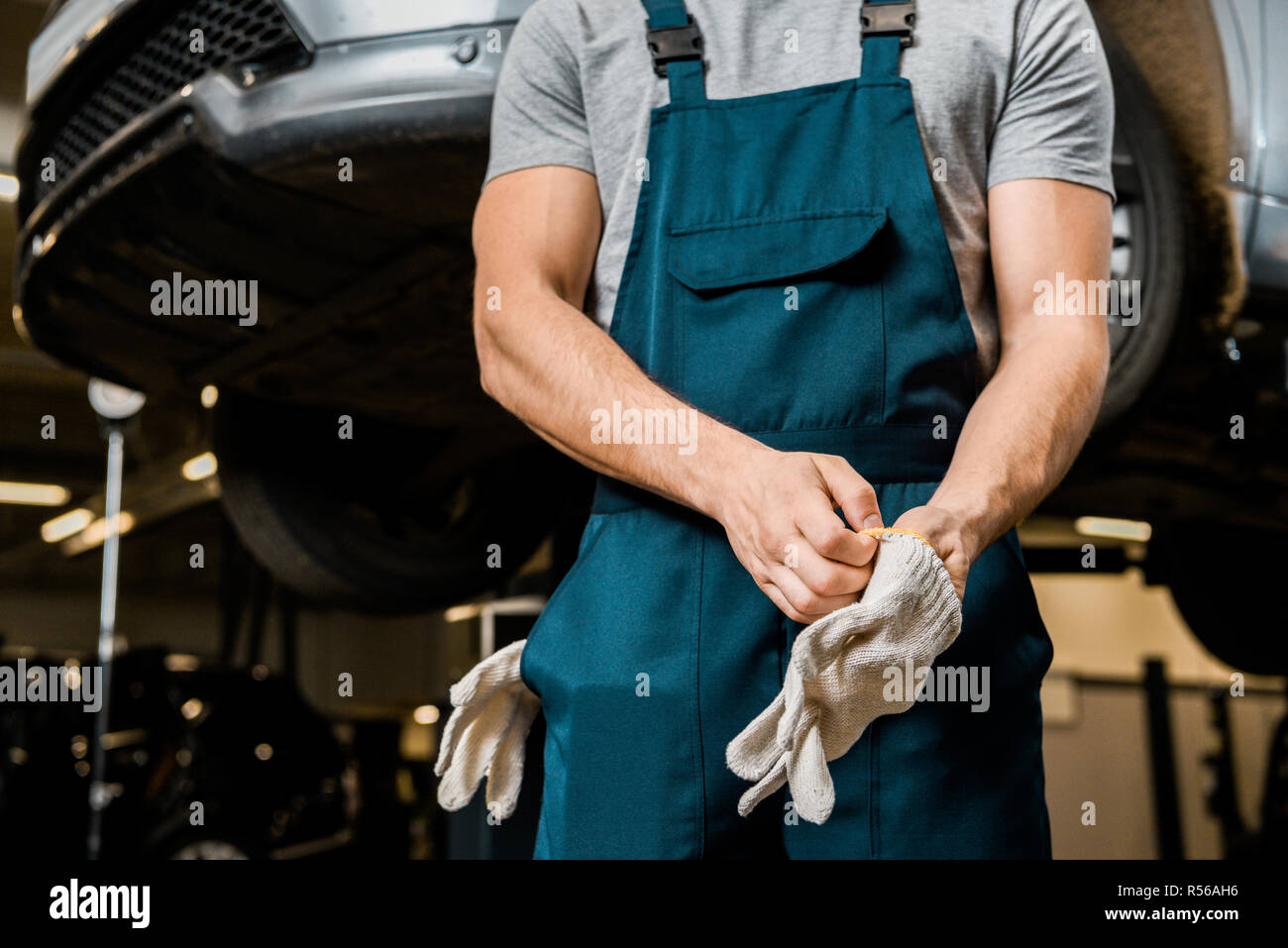 Vista parcial de la mecánica automotriz en uniforme usando guantes  protectores al taller de reparación de automóviles Fotografía de stock -  Alamy
