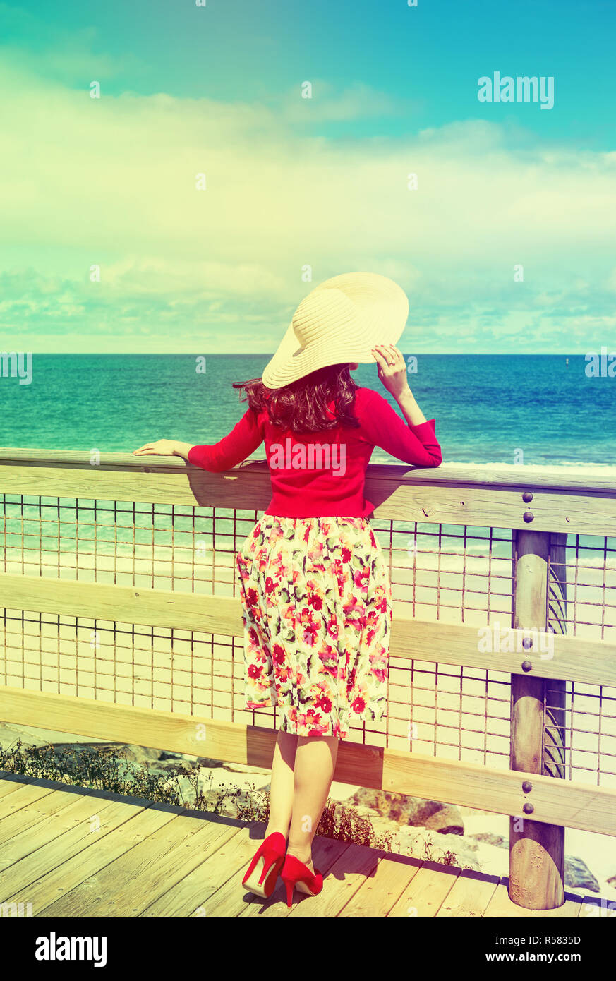 Bella mujer en rojo de pie y mirando al mar en estilo retro Foto de stock