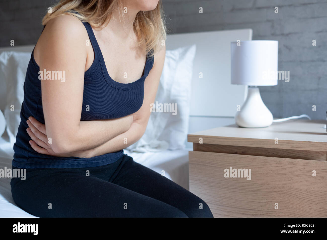 Mujer sufre dolores de estómago sentada en la cama Foto de stock