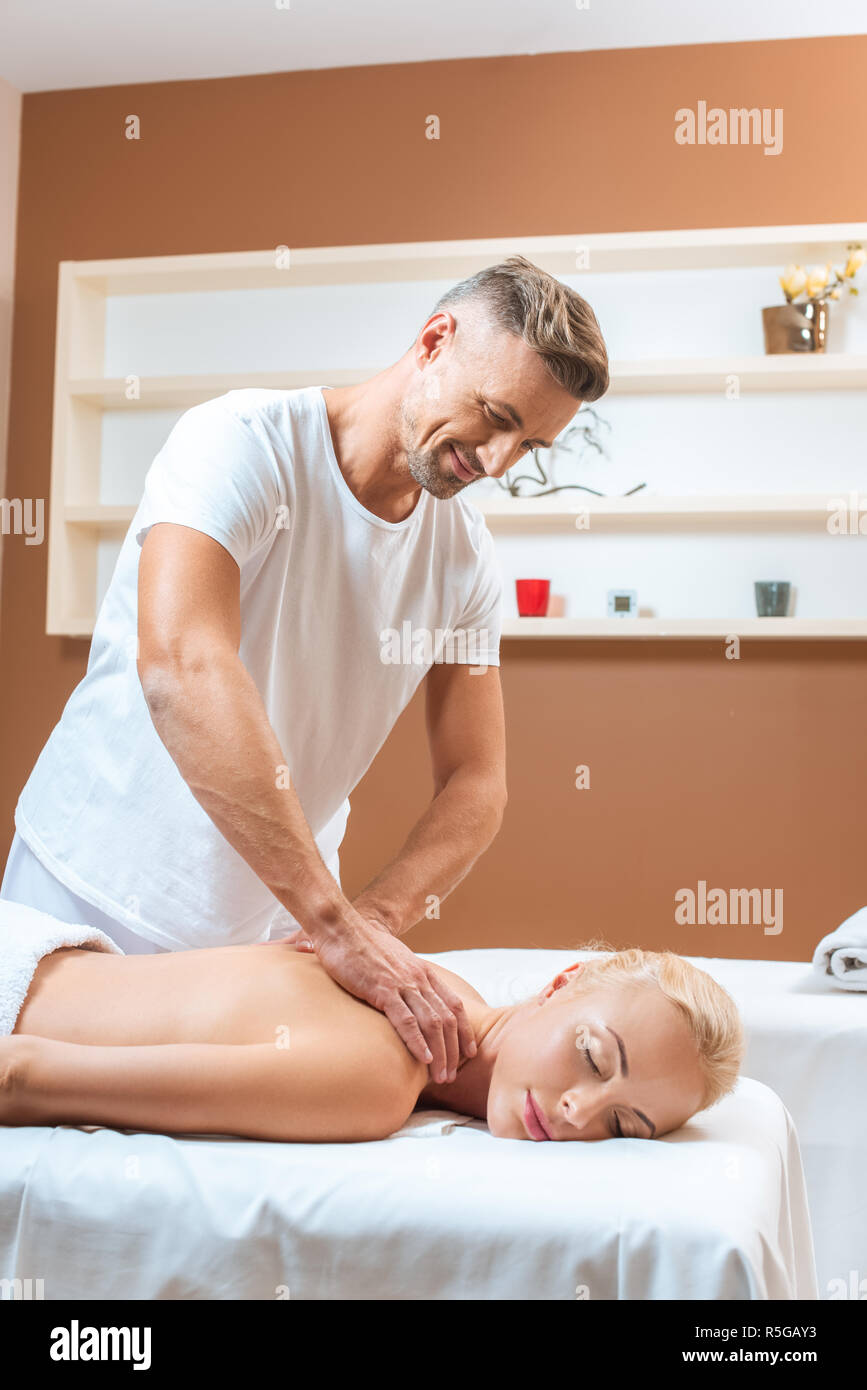 Guapo masajista haciendo masaje para mujer rubia en el salón spa Fotografía  de stock - Alamy