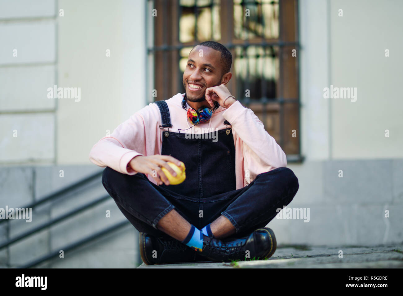 Joven negro comiendo una manzana sentado en pasos urbanos. Concepto de estilo de vida. Foto de stock