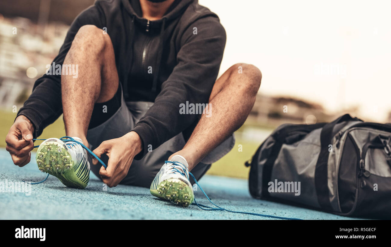 Atleta vistiendo zapatillas deportivas preparándose para la formación.  Captura recortada de un corredor sentado sobre una pista de atletismo de  encaje zapata atado con una bolsa por su lado Fotografía de stock 