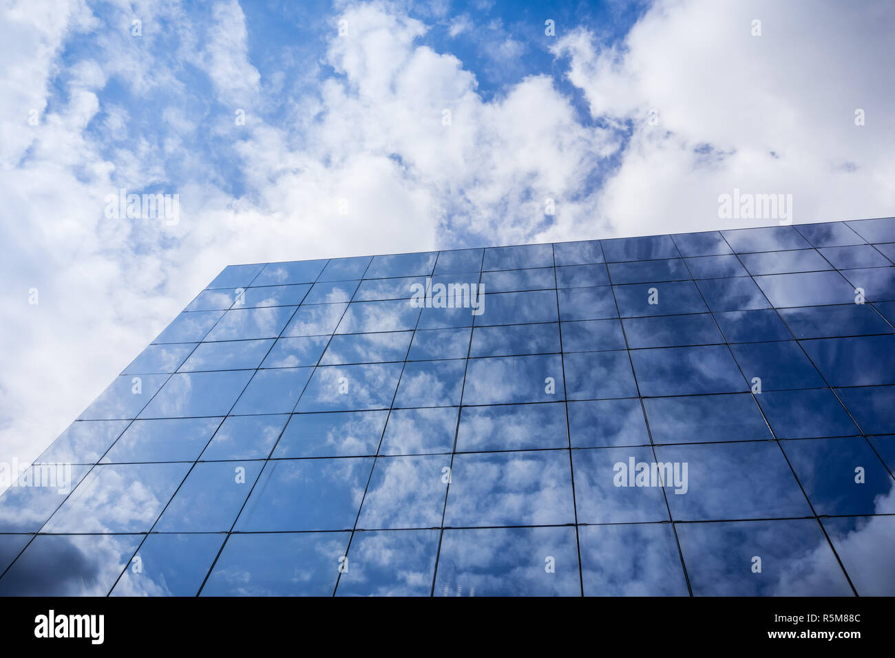 Las nubes blancas reflejan en la fachada de un moderno edificio de oficinas en un día soleado Foto de stock