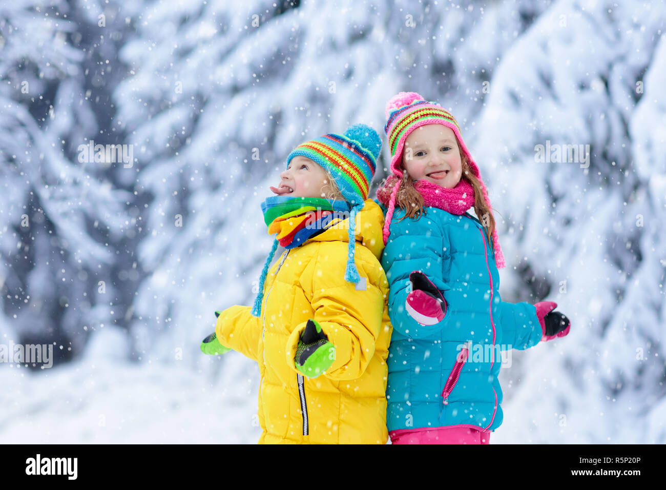 Niños jugando con nieve en invierno. Niña y Niño en la colorida chaqueta y gorro de punto atrapar los copos de nieve en Winter Park en Navidad. Los niños Fotografía