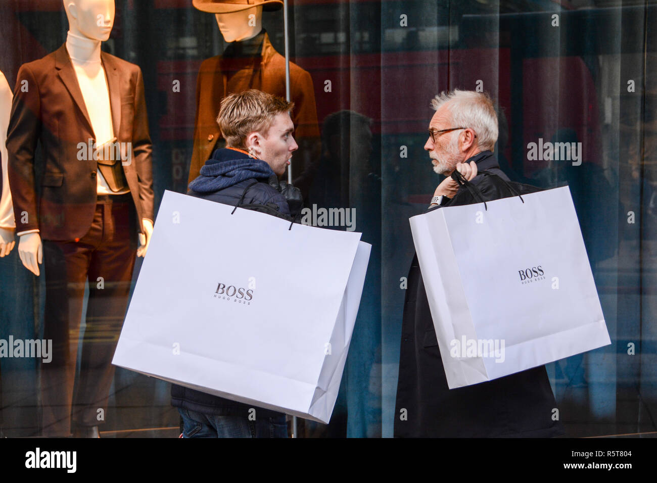 Dos compradores masculinos en una concurrida calle Oxford llevar grandes  bolsas de papel de Hugo Boss sobre sus hombros Fotografía de stock - Alamy