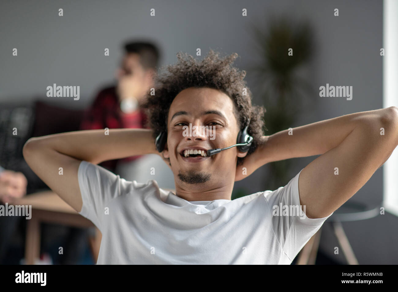 Satisfecho relajado africano-americanos freelancer sentirse feliz en el trabajo, sentado en la oficina con los auriculares. Foto de stock